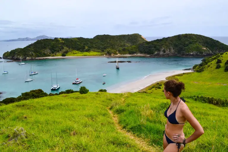 girl in bikini standing on green hill with bay in background