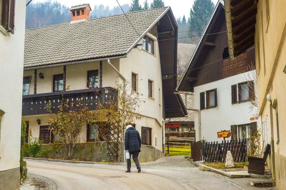 old lady carrying milk pail past alpine houses