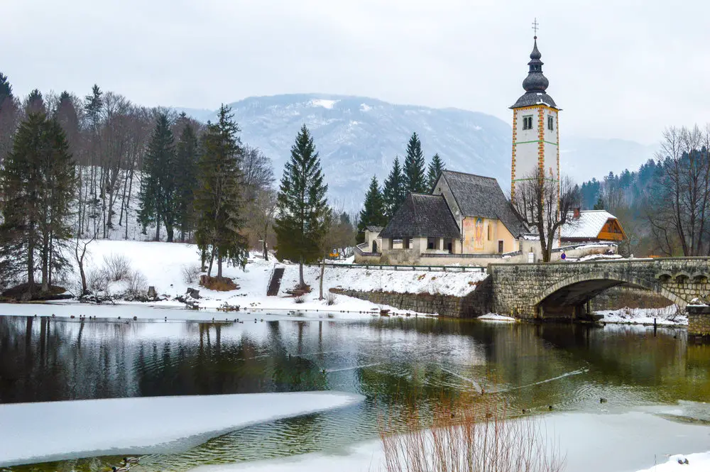 frozen stream with church and pine trees - is Slovenia worth visiting?