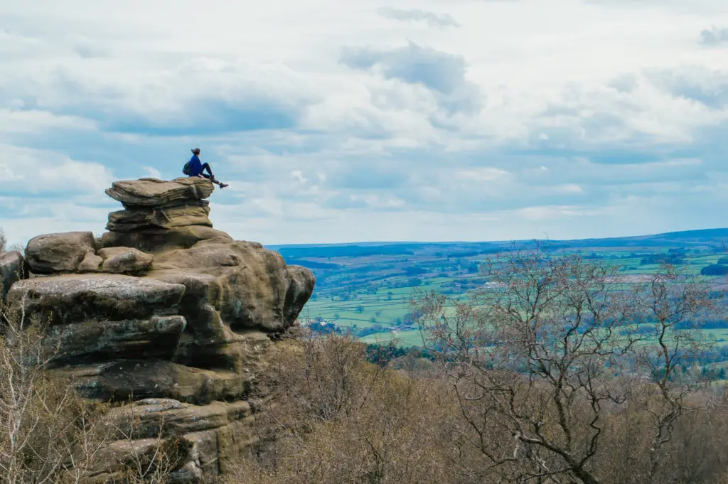 girl sitting on precarious rock overlooking fields