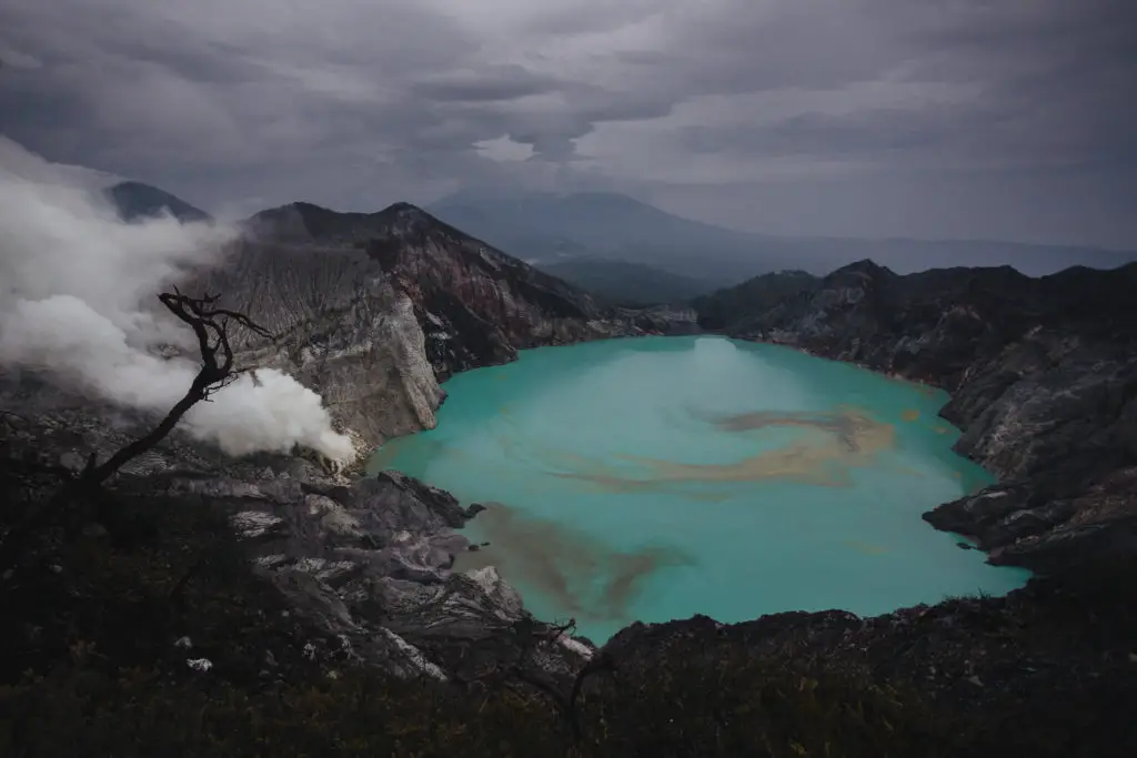 blue lake in black crater with white steam