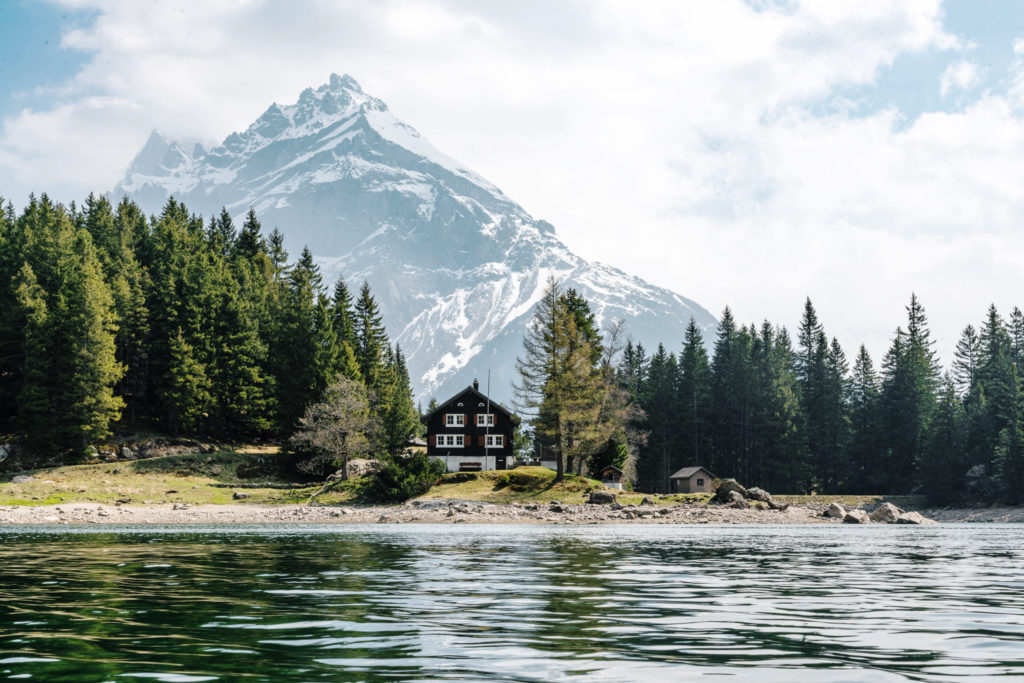 swiss house on lakefront surrounded by trees and a mountain