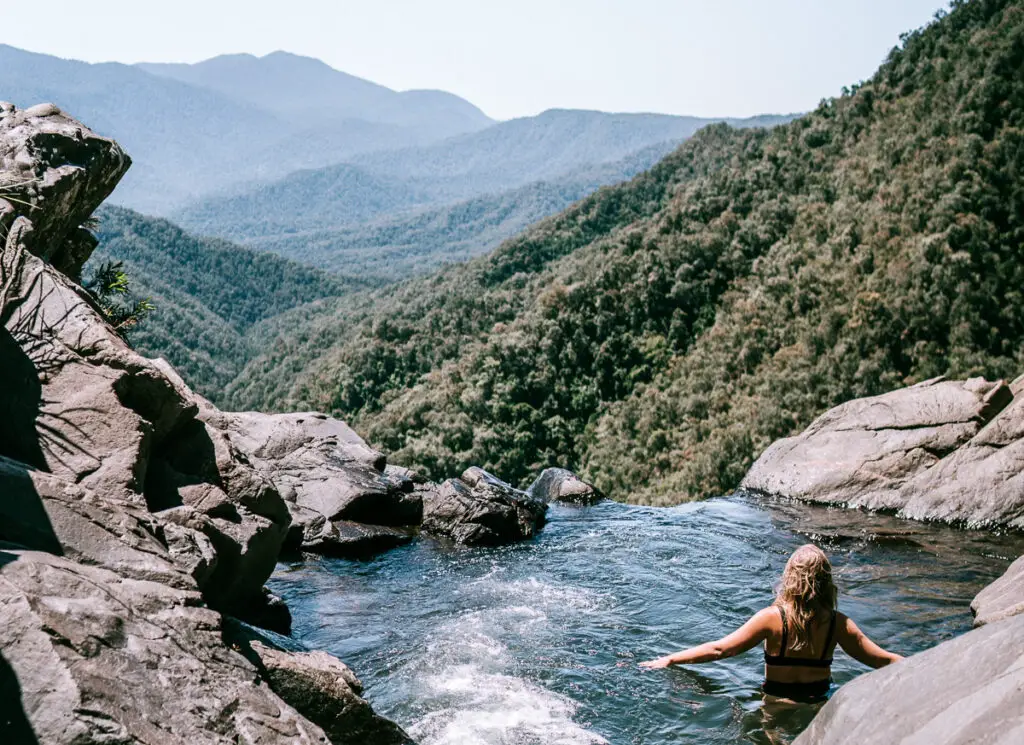 girl in waterfall rock pool overlooking mountains