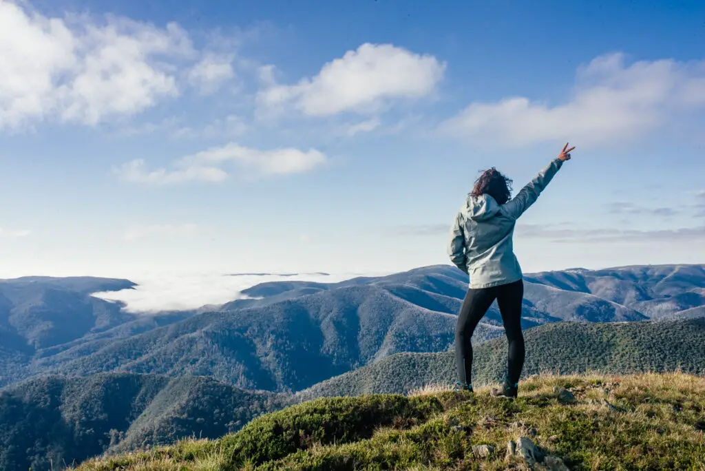 girl standing on top of mountain with arm up in the air with peace sign