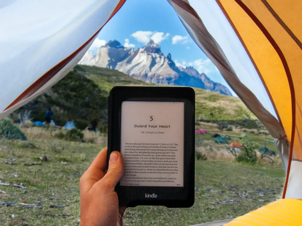hand holding kindle in tent with mountain backdrop