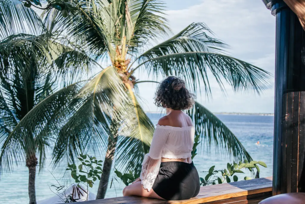 girl sat on bench in front of sea and palm trees in a resort