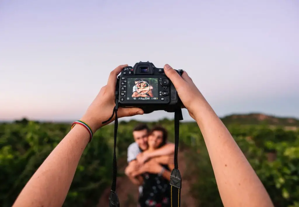 hand holding camera with couple having a photoshoot