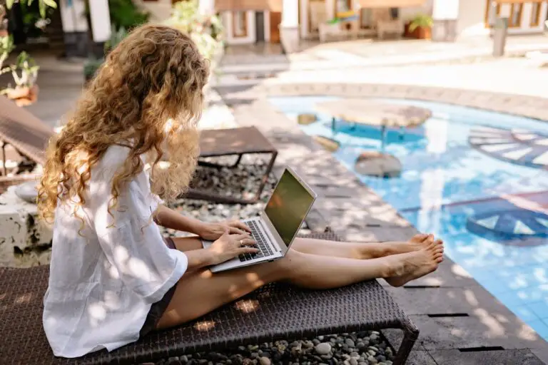 girl on laptop sat by swimming pool