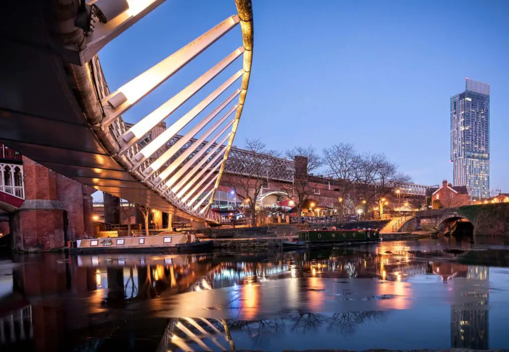 modern curved bridge and quayside in manchester at night with lights reflected in the water