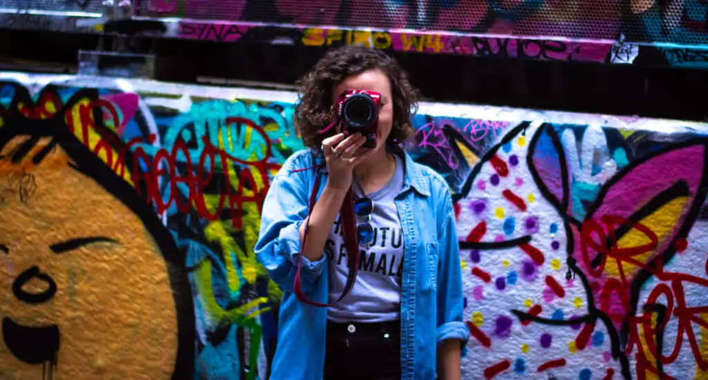 girl in front of graffiti wall with a red camera over her face