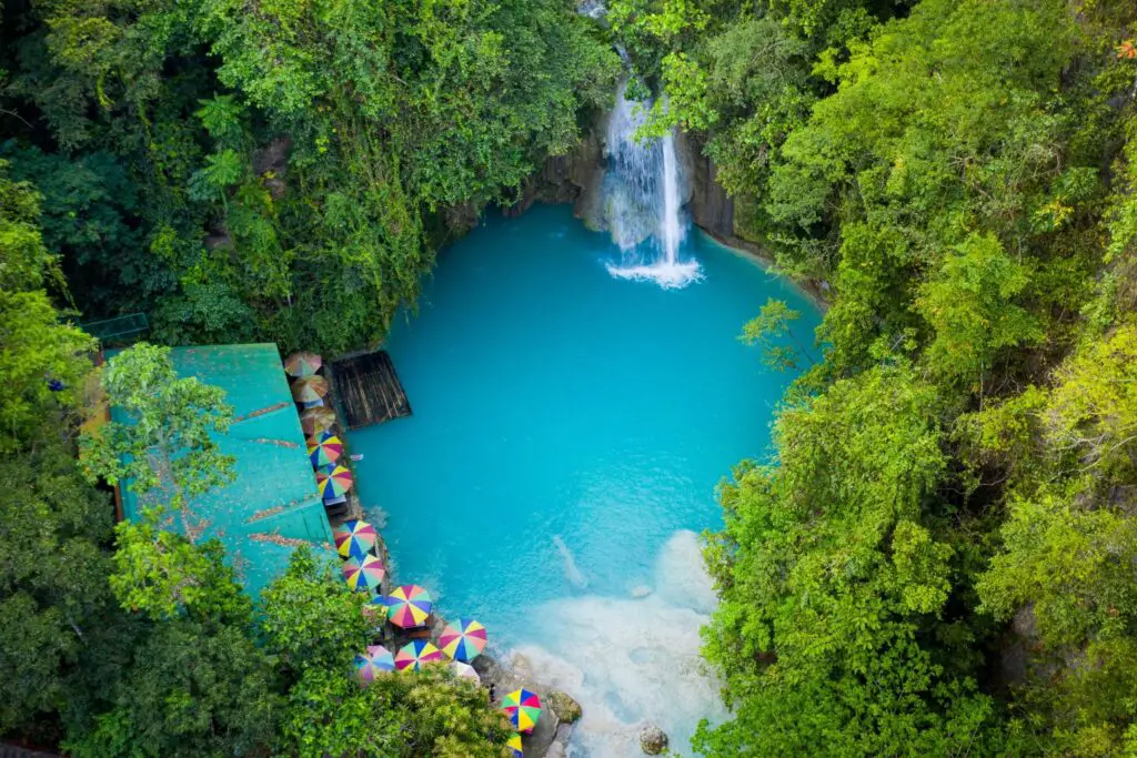 milky blue water with waterfall surrounded by green vegetation